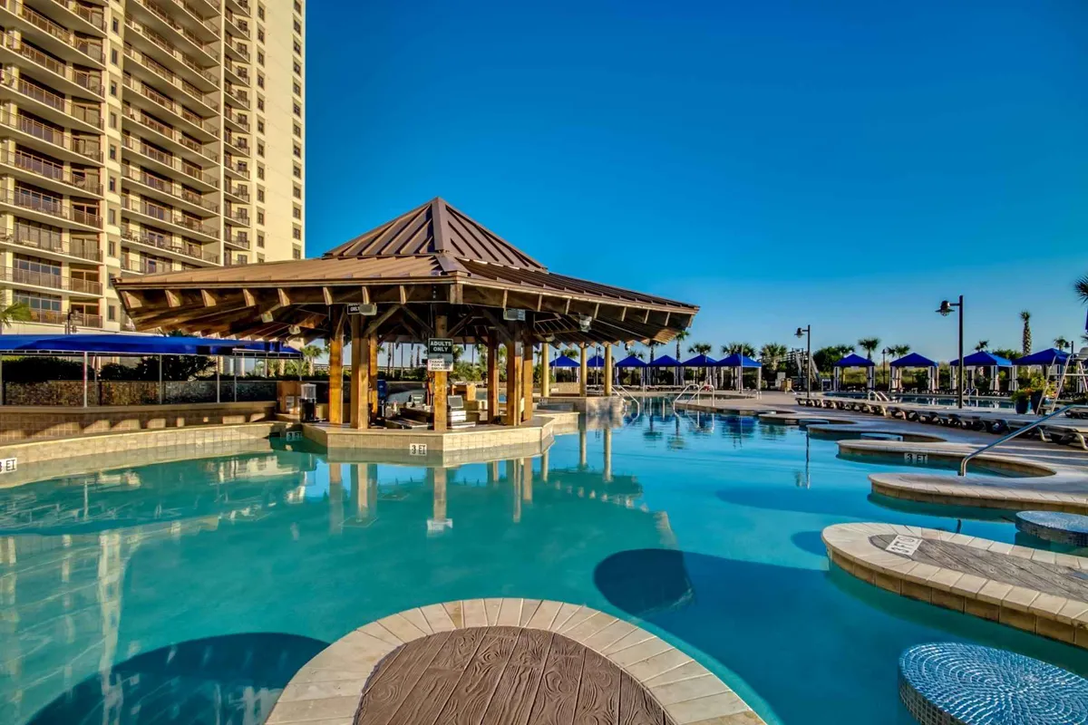 This exterior shot captures the resort's swimming pool area, featuring a pool cabana, sparkling blue water, and several lounge chairs arranged for sunbathing. The scene suggests a relaxed, fun-filled atmosphere ideal for families enjoying poolside activities under the sun or shade.