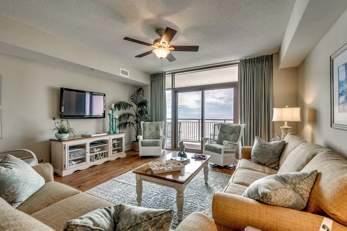 A spacious and inviting living room featuring large windows that flood the space with natural light and offer expansive ocean views. Comfortable seating surrounds a decorative coffee table, ideal for group gatherings, board games, and movie nights. The layout suggests a seamless connection to the outdoors, inviting the sea breeze inside.